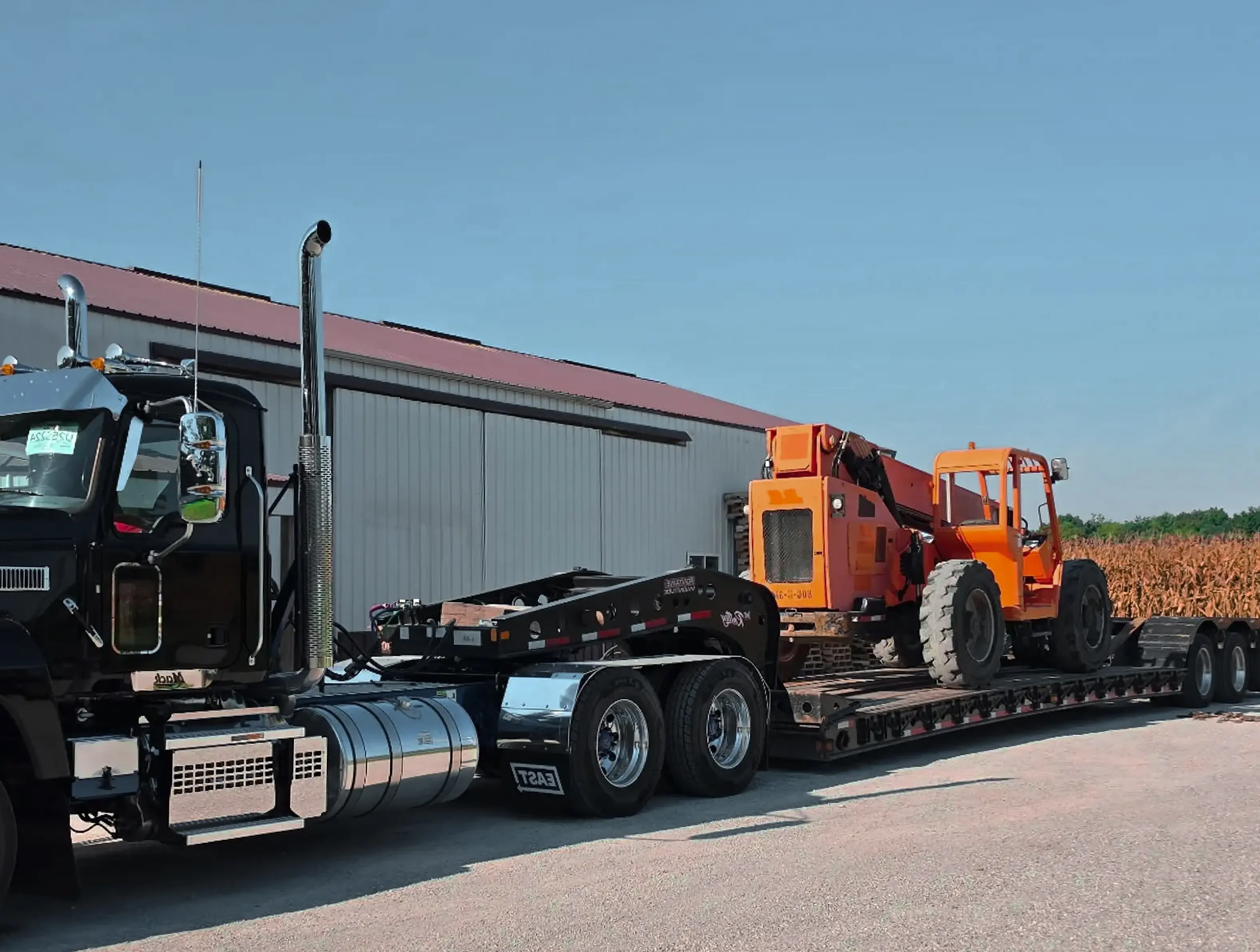 heavy-duty semi-truck pulling a lowboy trailer loaded with a construction telehandler