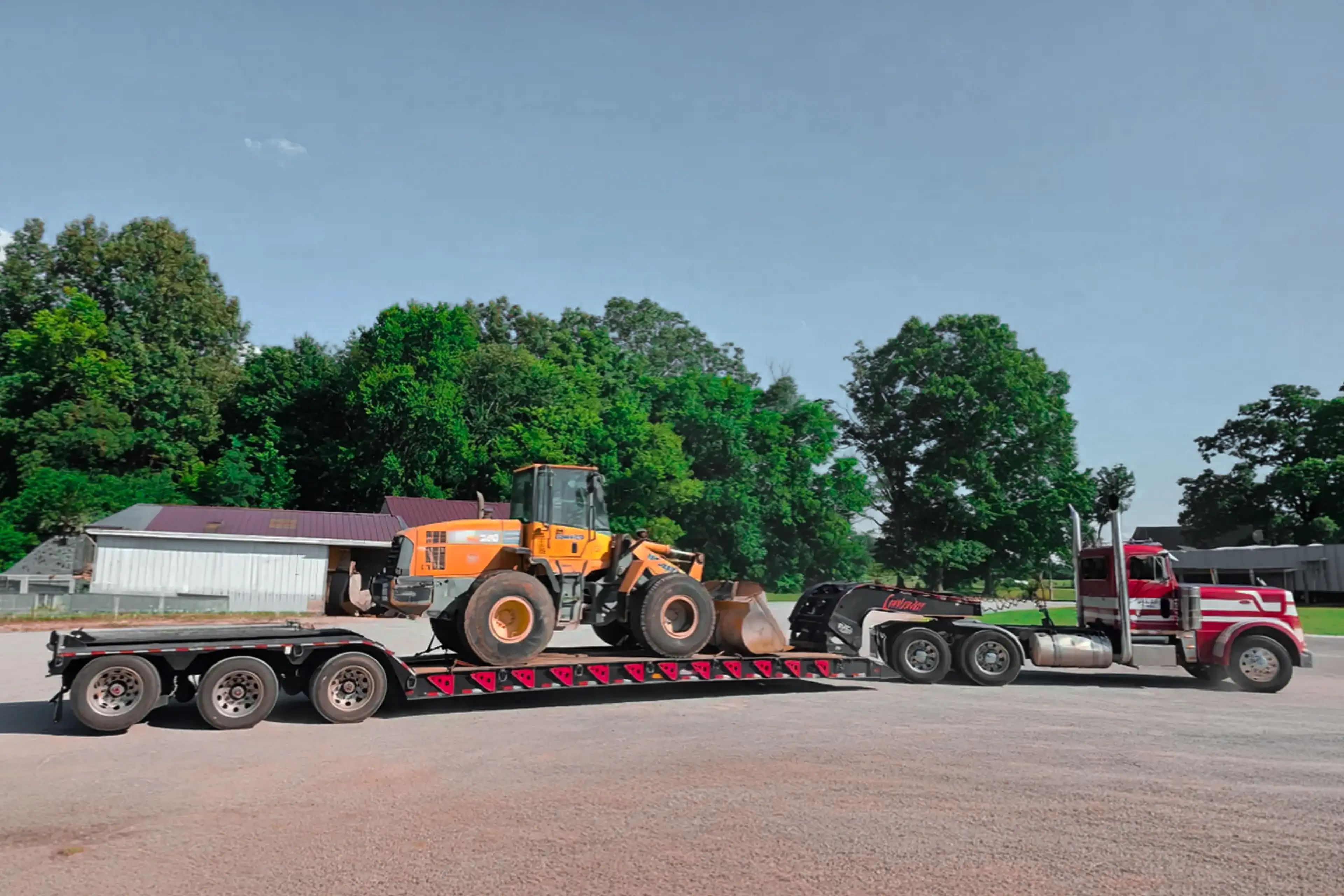 The image shows a heavy-duty semi-truck hauling a yellow wheel loader on a trailer
